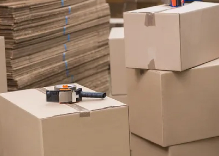 Cardboard packing boxes, flat and assembled, with a box tape gun.